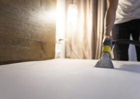 Man cleans the mattress from dust and dirt with washing vacuum cleaner. Bed cleaning process